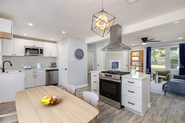 kitchen featuring island range hood, sink, white cabinets, hanging light fixtures, and stainless steel appliances