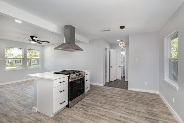 kitchen featuring wood-type flooring, decorative light fixtures, island range hood, stainless steel range with gas cooktop, and white cabinets