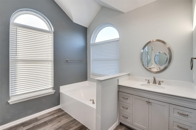 full bathroom with baseboards, lofted ceiling, wood finished floors, a garden tub, and vanity