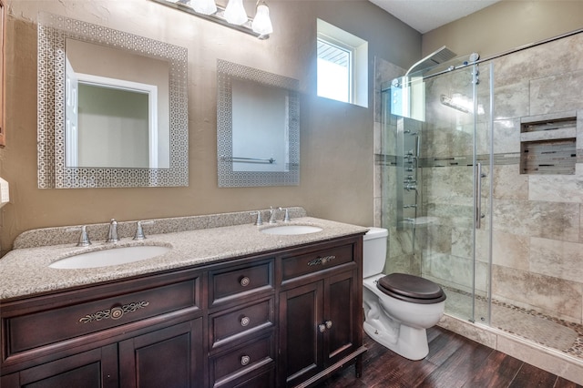 full bath with double vanity, a sink, a shower stall, and wood finished floors