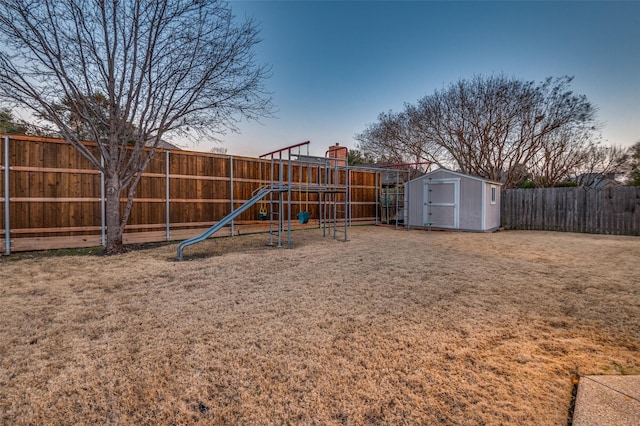 playground at dusk featuring a storage shed, a fenced backyard, an outbuilding, a yard, and a playground