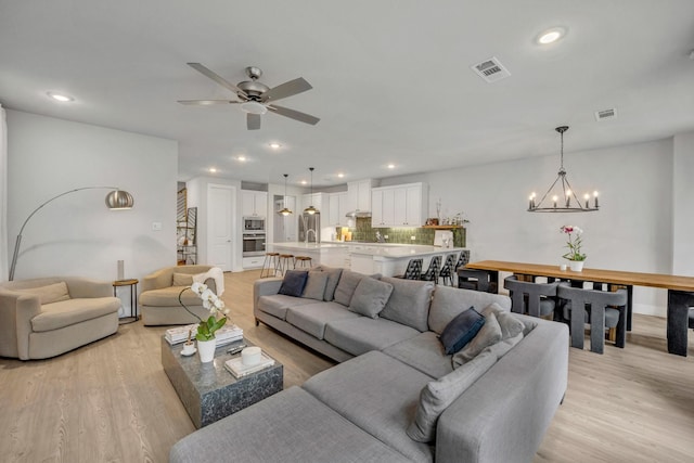 living room with ceiling fan with notable chandelier and light hardwood / wood-style floors