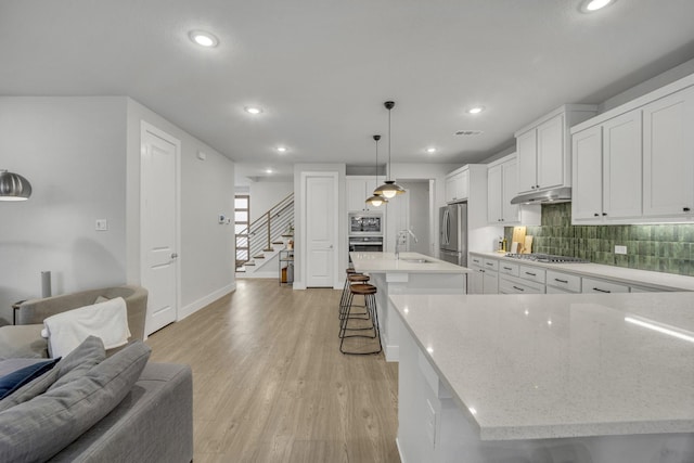 kitchen featuring sink, appliances with stainless steel finishes, a spacious island, white cabinets, and decorative light fixtures