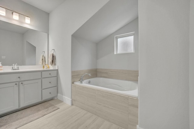 bathroom featuring vanity, tiled tub, and lofted ceiling