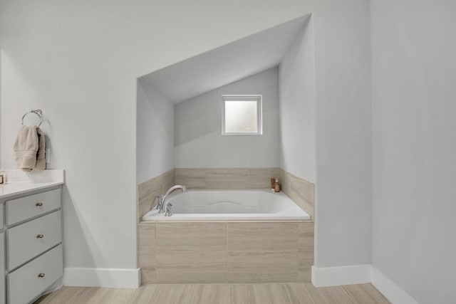 bathroom with vaulted ceiling, vanity, hardwood / wood-style floors, and tiled tub