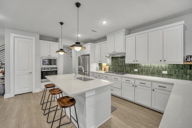 kitchen featuring sink, white cabinetry, light wood-type flooring, pendant lighting, and stainless steel appliances