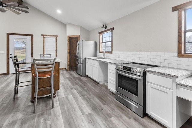 kitchen with light stone counters, appliances with stainless steel finishes, vaulted ceiling, and white cabinets