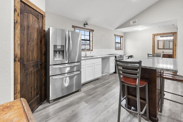 kitchen with sink, stainless steel fridge, white cabinetry, light stone countertops, and a kitchen island