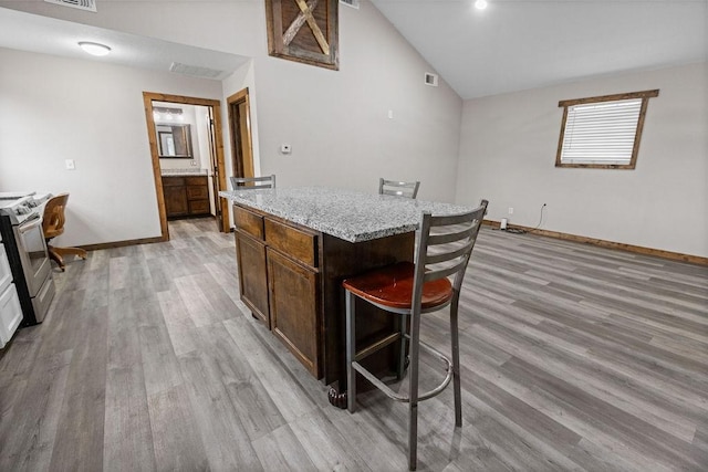 kitchen featuring a kitchen island, a breakfast bar, lofted ceiling, light hardwood / wood-style floors, and stainless steel electric range