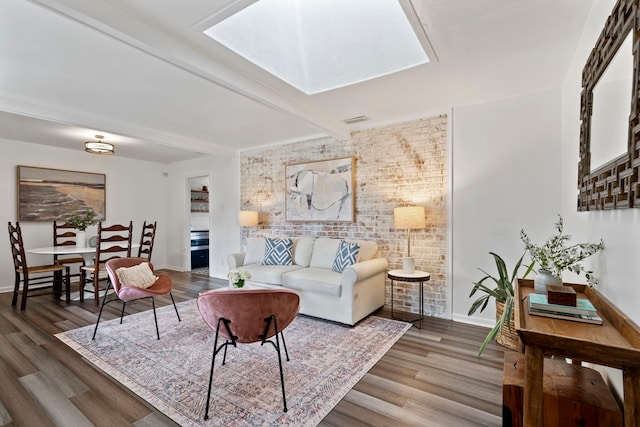 living room featuring beamed ceiling, wood-type flooring, brick wall, and a skylight