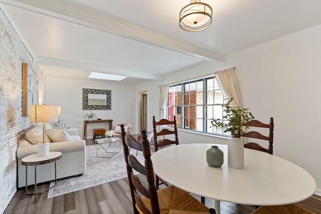 dining space with hardwood / wood-style floors, a skylight, and beamed ceiling