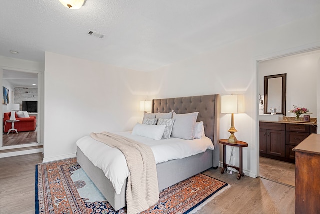 bedroom with ensuite bath, a textured ceiling, and light wood-type flooring