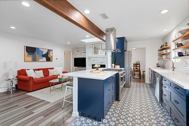 kitchen featuring sink, a kitchen bar, island exhaust hood, stainless steel appliances, and blue cabinetry