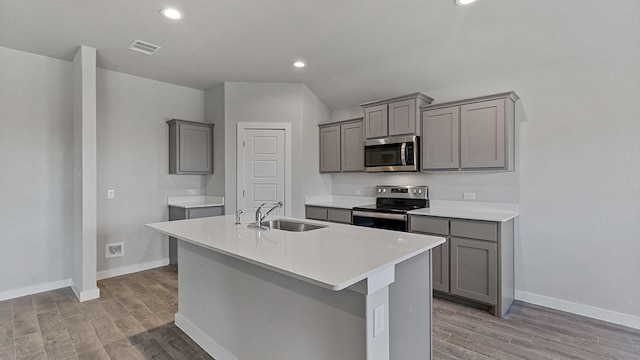 kitchen with stainless steel appliances, sink, a kitchen island with sink, and light wood-type flooring