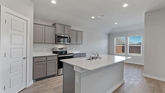 kitchen featuring sink, gray cabinets, appliances with stainless steel finishes, an island with sink, and light wood-type flooring