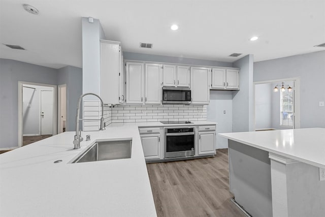 kitchen with sink, light hardwood / wood-style flooring, white cabinetry, backsplash, and stainless steel appliances