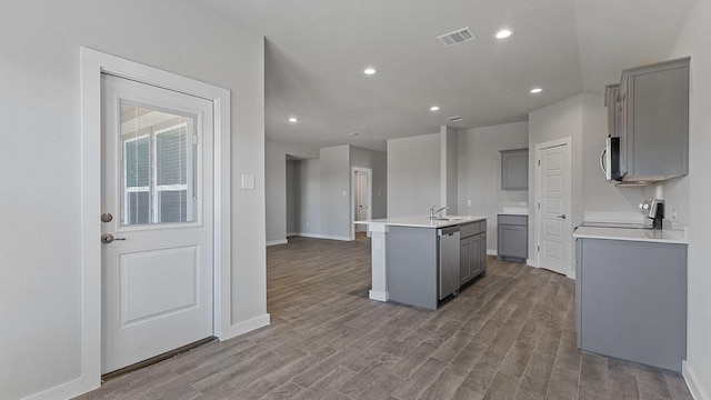 kitchen with a kitchen island with sink, hardwood / wood-style floors, gray cabinets, and stainless steel appliances