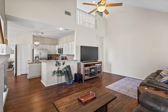 living room with dark hardwood / wood-style flooring, ceiling fan with notable chandelier, and a towering ceiling