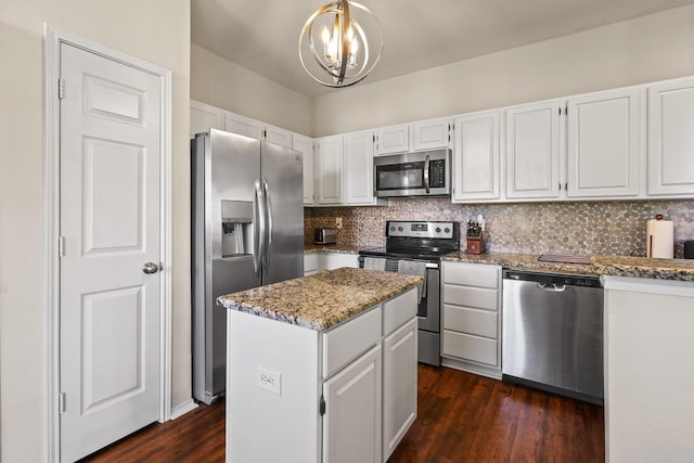 kitchen with hanging light fixtures, a kitchen island, white cabinets, stainless steel appliances, and backsplash