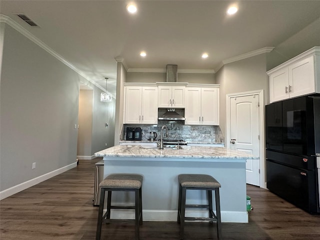 kitchen with black fridge, a kitchen island with sink, white cabinets, and backsplash