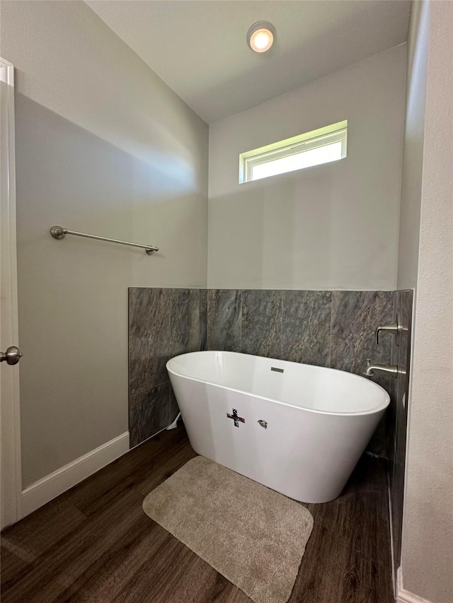 bathroom with tile walls, a tub to relax in, and hardwood / wood-style floors