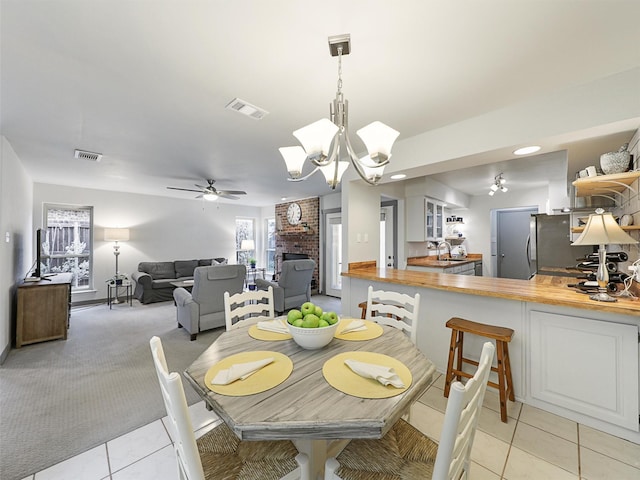 dining room featuring a brick fireplace, ceiling fan with notable chandelier, and light carpet