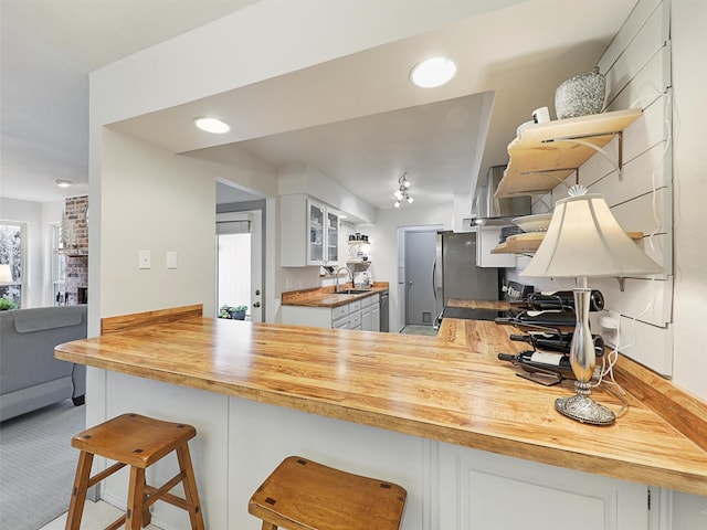 kitchen featuring white cabinetry, wood counters, kitchen peninsula, and sink