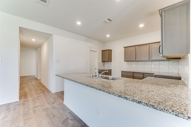 kitchen featuring sink, light hardwood / wood-style flooring, light stone counters, tasteful backsplash, and kitchen peninsula