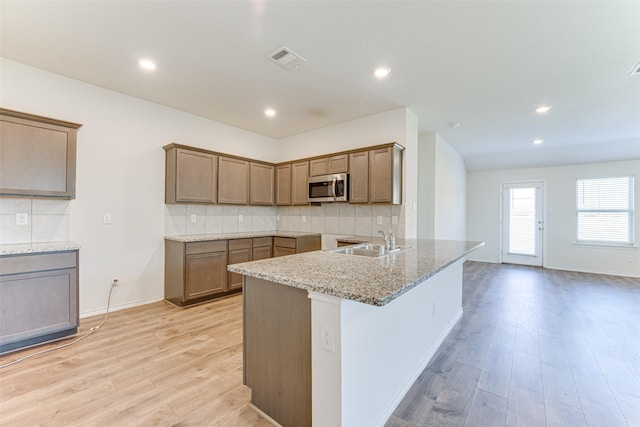 kitchen featuring sink, tasteful backsplash, light stone countertops, light hardwood / wood-style floors, and kitchen peninsula