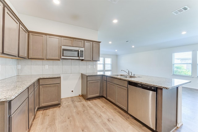 kitchen featuring sink, light hardwood / wood-style flooring, appliances with stainless steel finishes, tasteful backsplash, and light stone countertops