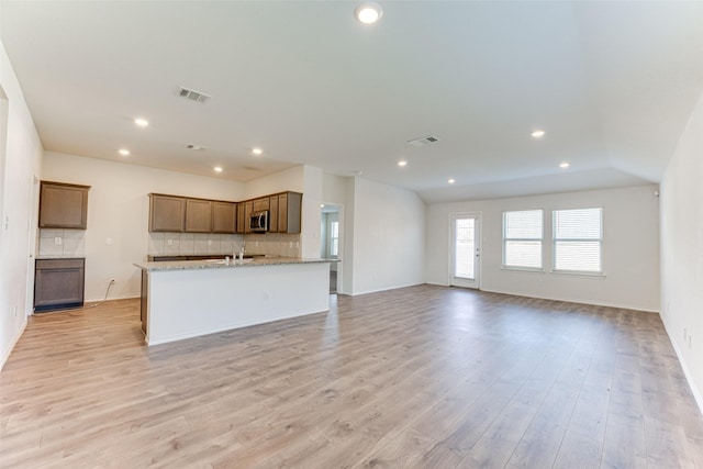 kitchen with tasteful backsplash, an island with sink, light stone countertops, and light hardwood / wood-style flooring