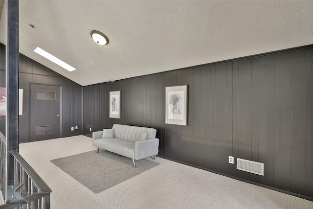 living area featuring light colored carpet, lofted ceiling with skylight, and a textured ceiling