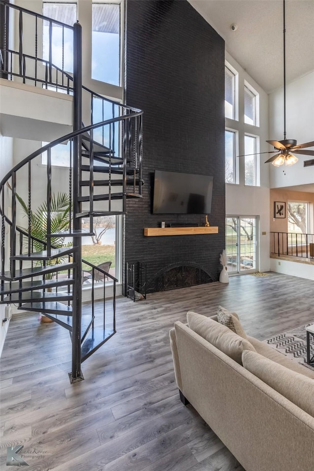 living room with ceiling fan, a towering ceiling, hardwood / wood-style floors, and a fireplace