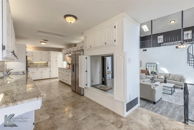 kitchen featuring stainless steel refrigerator with ice dispenser, white cabinetry, sink, and light stone counters