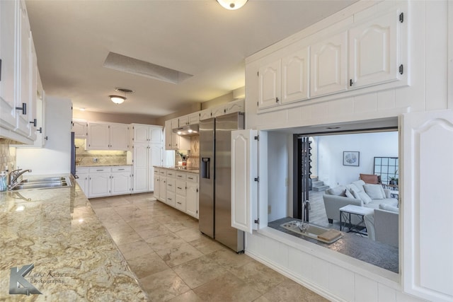 kitchen with sink, light stone counters, stainless steel fridge, decorative backsplash, and white cabinets