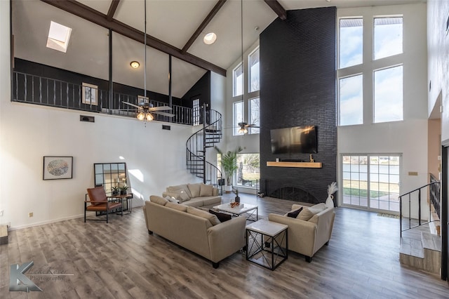 living room featuring high vaulted ceiling, a large fireplace, beamed ceiling, ceiling fan, and hardwood / wood-style floors