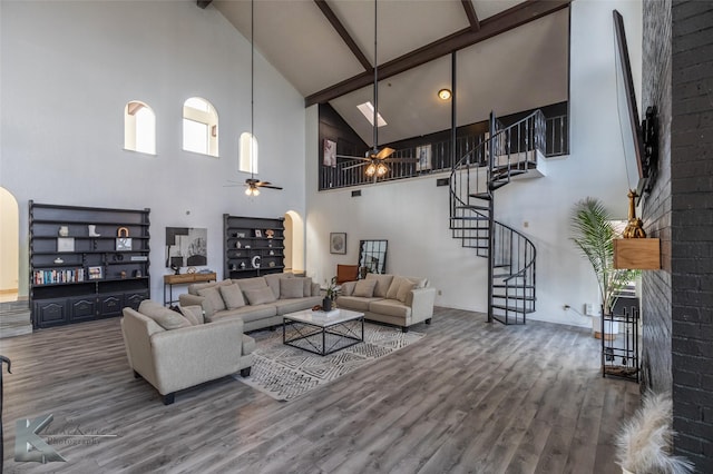 living room featuring hardwood / wood-style flooring, beamed ceiling, ceiling fan, and a towering ceiling