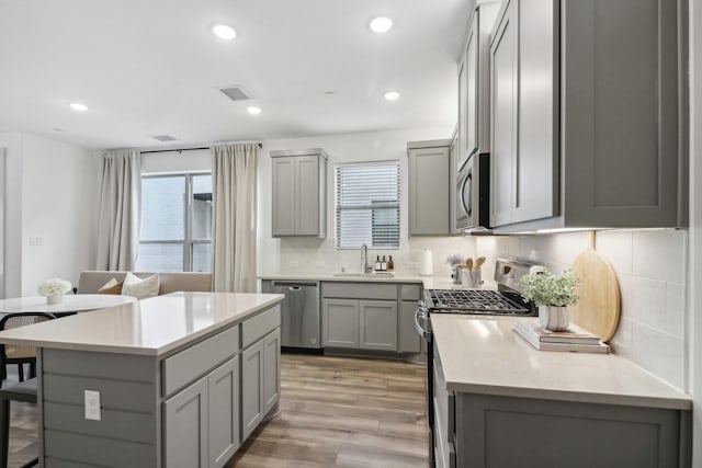 kitchen with a sink, stainless steel appliances, gray cabinets, and a kitchen breakfast bar