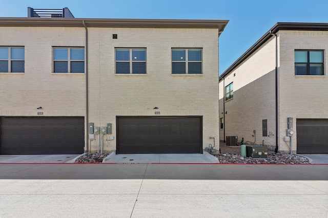 rear view of house with a garage, central AC, brick siding, and concrete driveway