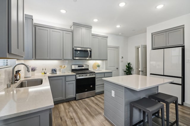 kitchen featuring tasteful backsplash, gray cabinetry, appliances with stainless steel finishes, a sink, and a kitchen bar