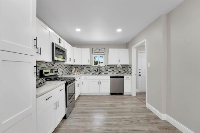 kitchen with sink, stainless steel appliances, white cabinets, decorative backsplash, and light wood-type flooring