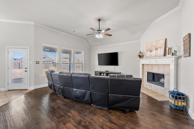 living room featuring a tiled fireplace, vaulted ceiling, ornamental molding, and hardwood / wood-style floors