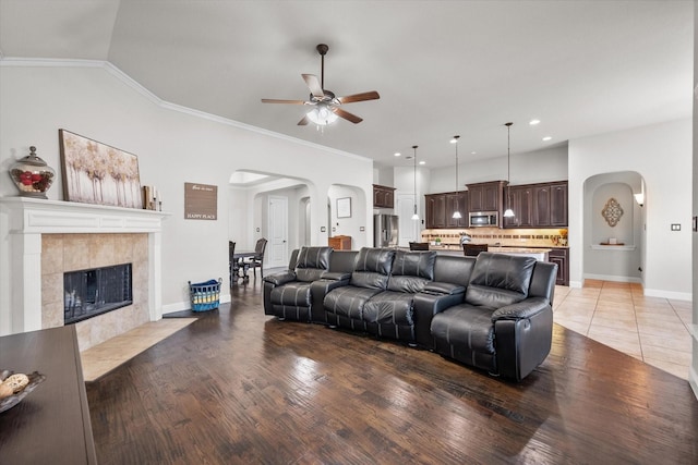 living room with crown molding, ceiling fan, wood-type flooring, and a tile fireplace