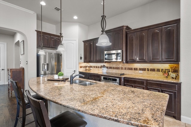 kitchen featuring stainless steel appliances, sink, a center island with sink, and dark brown cabinetry