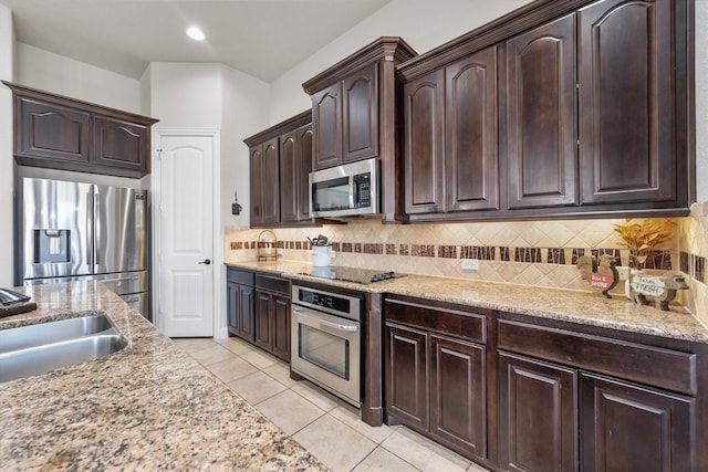 kitchen with light stone counters, a sink, stainless steel appliances, dark brown cabinetry, and backsplash