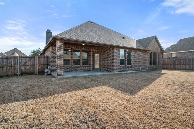 rear view of property with a fenced backyard, a patio, a chimney, and brick siding