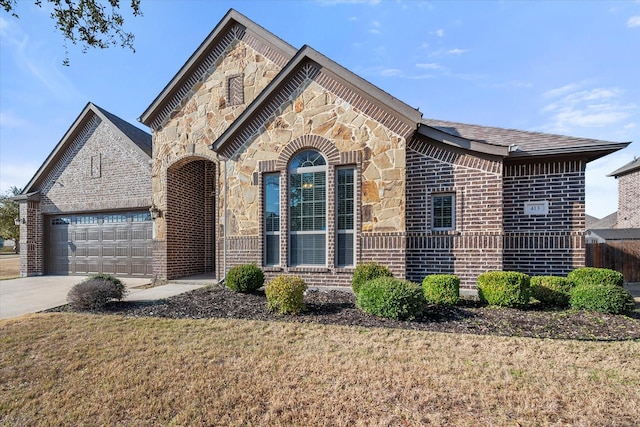 french country style house with concrete driveway, a front lawn, a garage, stone siding, and brick siding