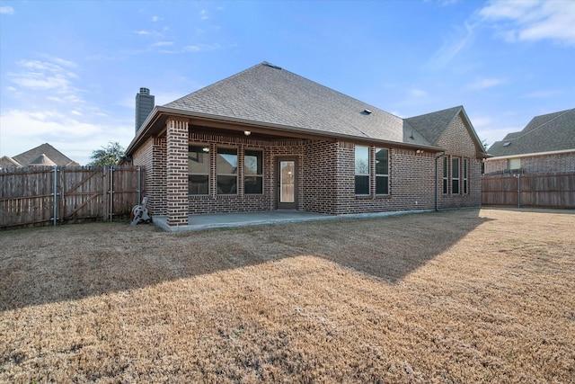 rear view of house with brick siding, roof with shingles, a chimney, a fenced backyard, and a patio