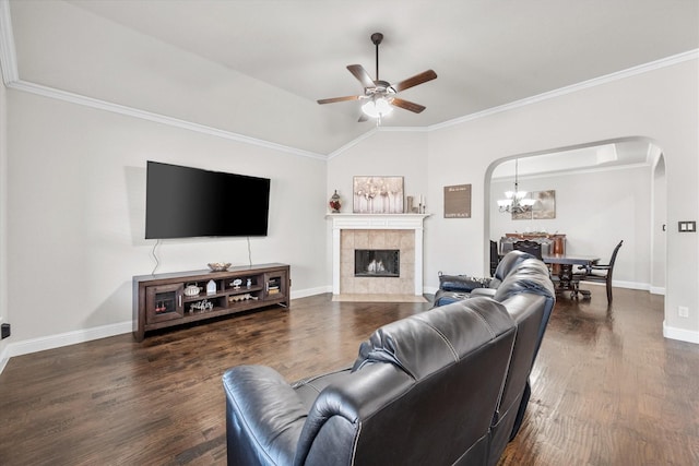 living room featuring crown molding, a tile fireplace, arched walkways, dark wood finished floors, and ceiling fan with notable chandelier