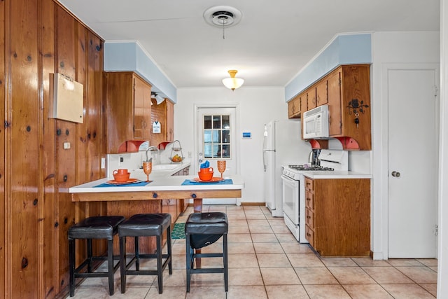 kitchen with a breakfast bar, sink, light tile patterned floors, kitchen peninsula, and white appliances